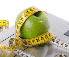 Tape measure around a green apple on a bathroom scales, isolated on white